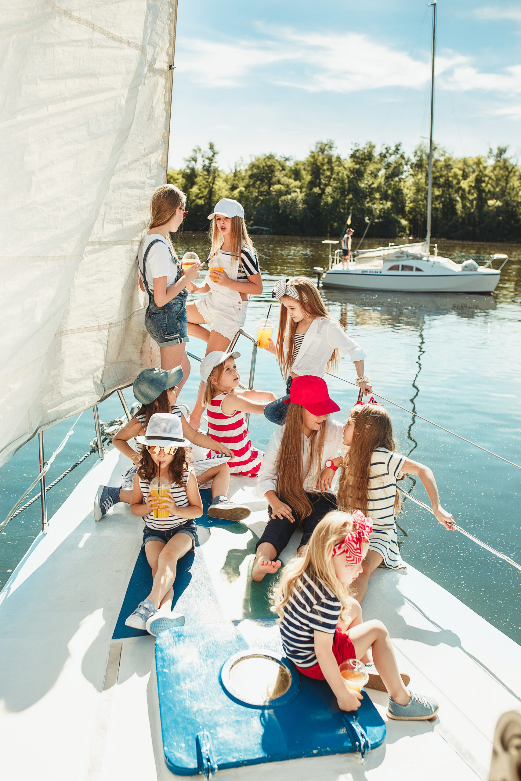 The children on board of sea yacht drinking orange juice. The teen or child girls against blue sky outdoor. Colorful clothes. Kids fashion, sunny summer, river and holidays concepts.